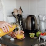 woman poring juice standing near table with fruits