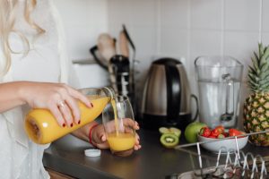 woman poring juice standing near table with fruits